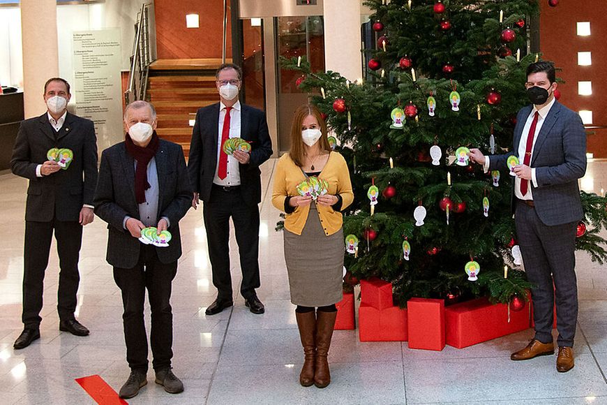 Personen stehen vor einem Weihnachtsbaum und tragen Maske