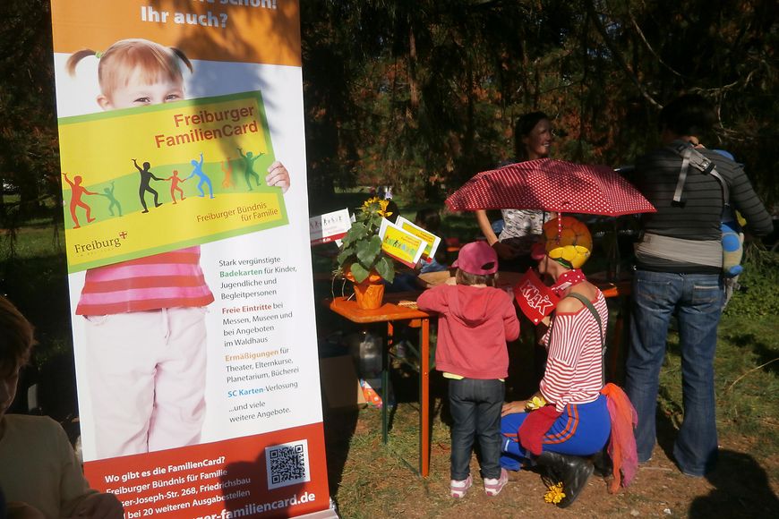 Eine als Clown verkleidete Frau und ein Kind stehen an einem Stand zum Weltkindertag in Freiburg